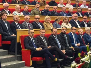 Uczestnicy oficjalnej uroczystości zasiadają w czerwonych fotelach audytorium.